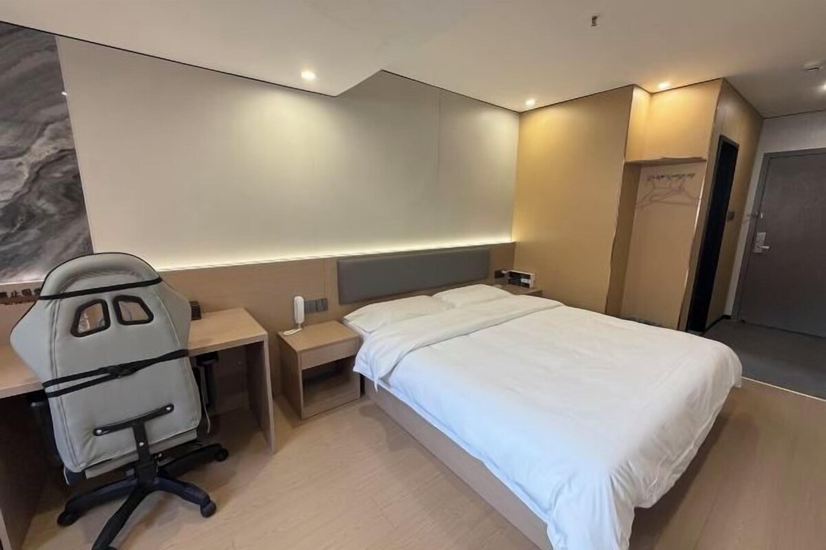 Quarto de hotel com uma cama, uma escrivaninha com cadeira, mesa de cabeceira e guarda-roupa.