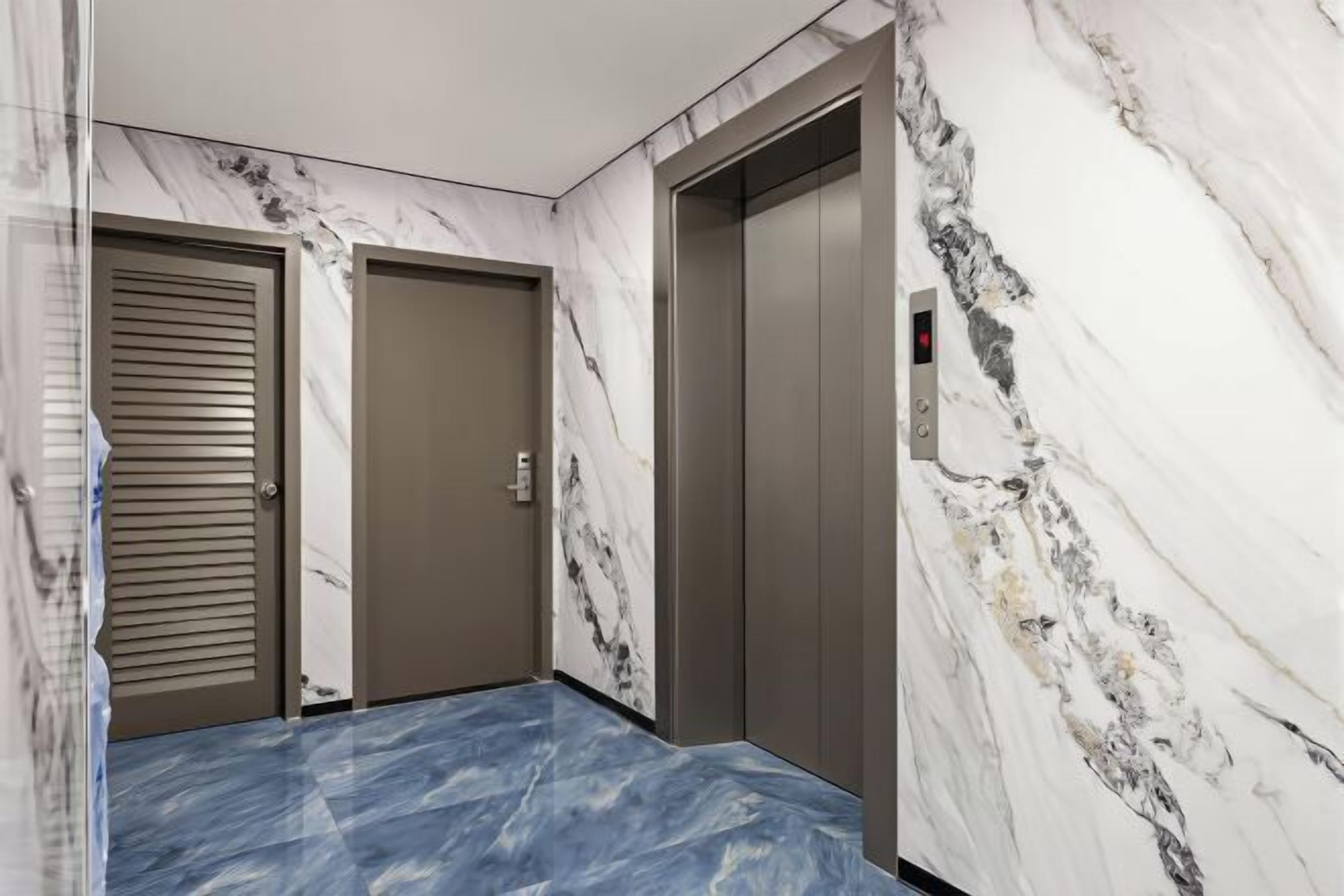 A hallway with marble walls and a blue marble floor, leading to two elevators.