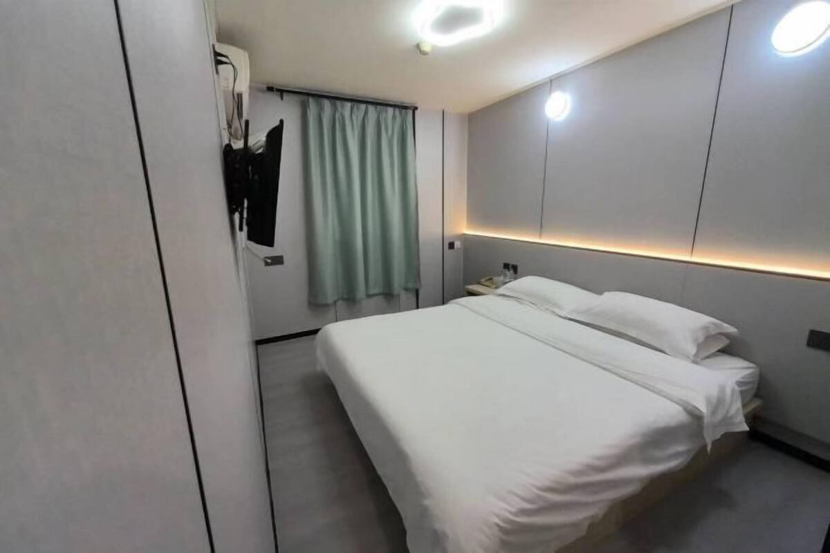 A modern hotel room with a neatly made bed, a bedside table, and a wall-mounted light fixture.