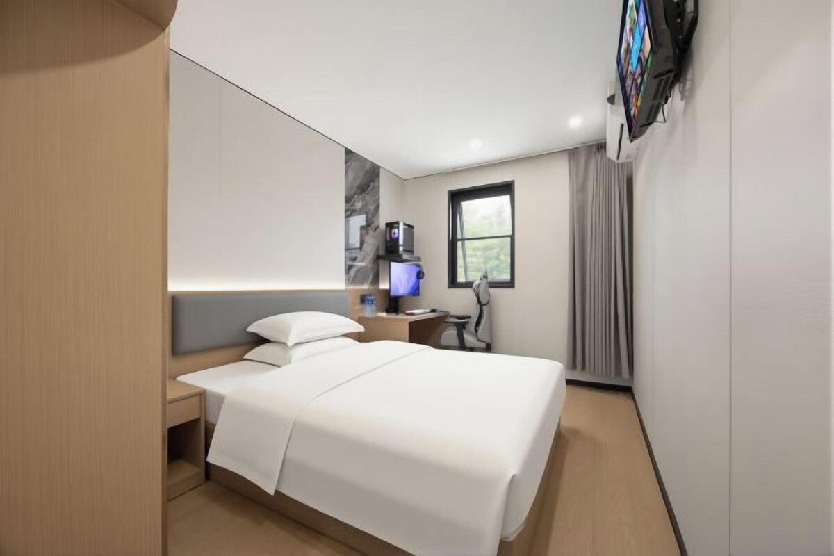 A hotel room with a bed, a desk, a TV, and a window.