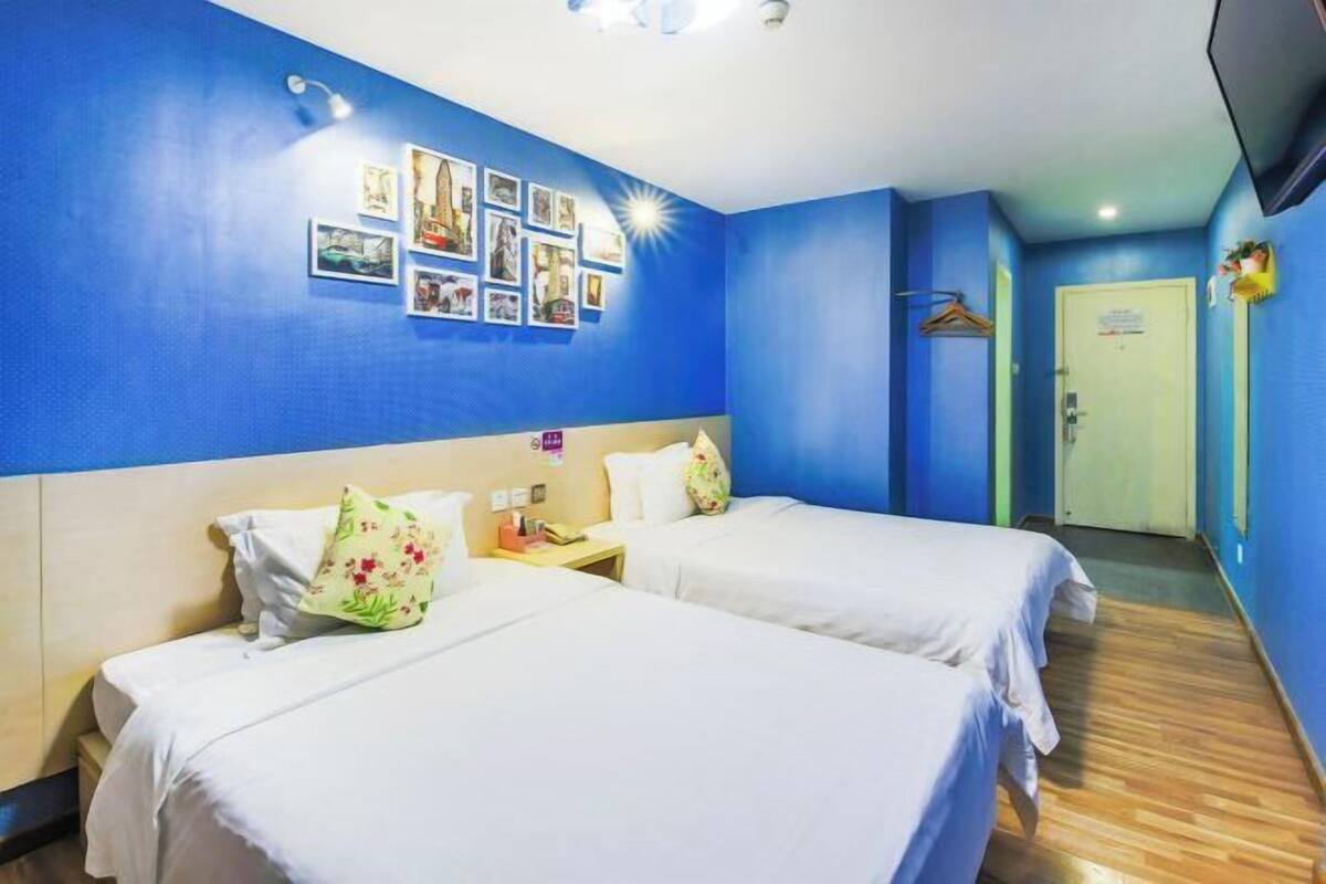 A hotel room with two beds, a wooden floor, a TV, and a door with a sign.