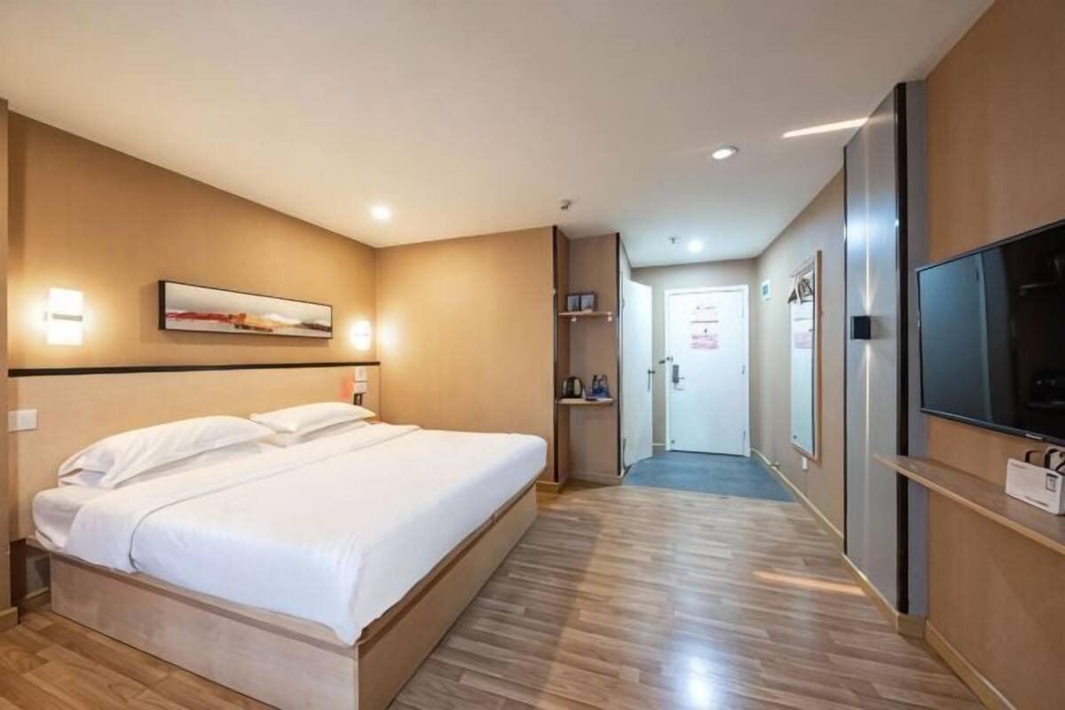 A hotel room with a bed, a television, a hallway, and a door.