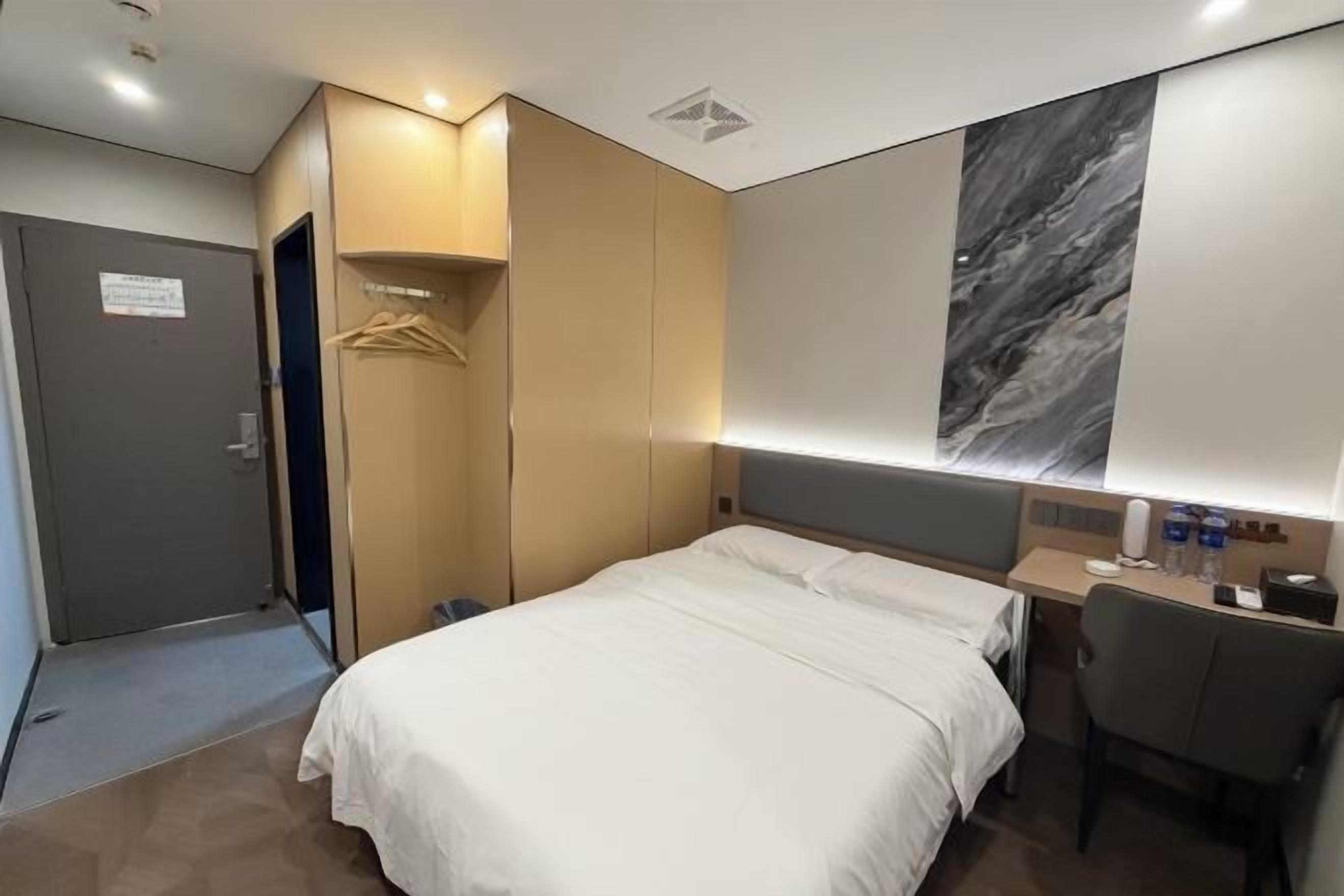 A hotel room with a bed, a desk, a chair, a wardrobe, and a wall-mounted artwork.