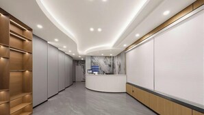 Un hall d’hôtel moderne avec un comptoir d’accueil, des étagères en bois et un mur en marbre.