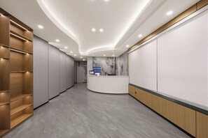 Un hall d’hôtel moderne avec un comptoir d’accueil, des étagères en bois et un mur en marbre.