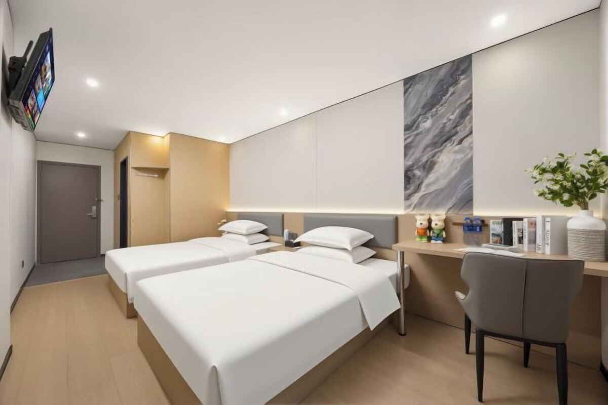 A hotel room with two beds, a desk, a chair, a TV, and a large mirror.