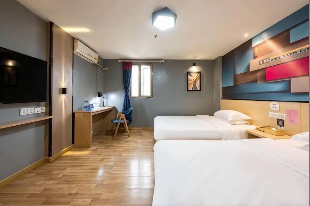 A hotel room with two beds, a desk with a chair, a TV, and a window with curtains.