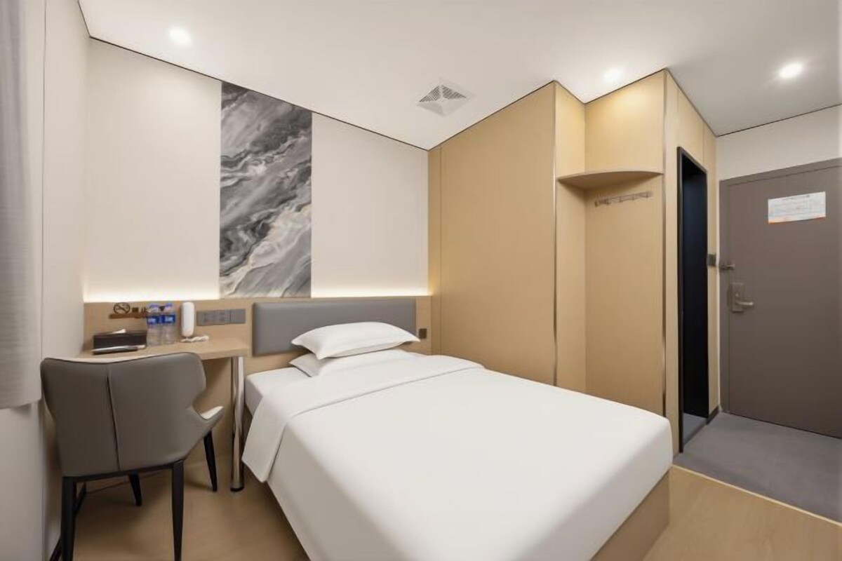 A hotel room with a bed, a desk, a chair, a marble wall, and a door.
