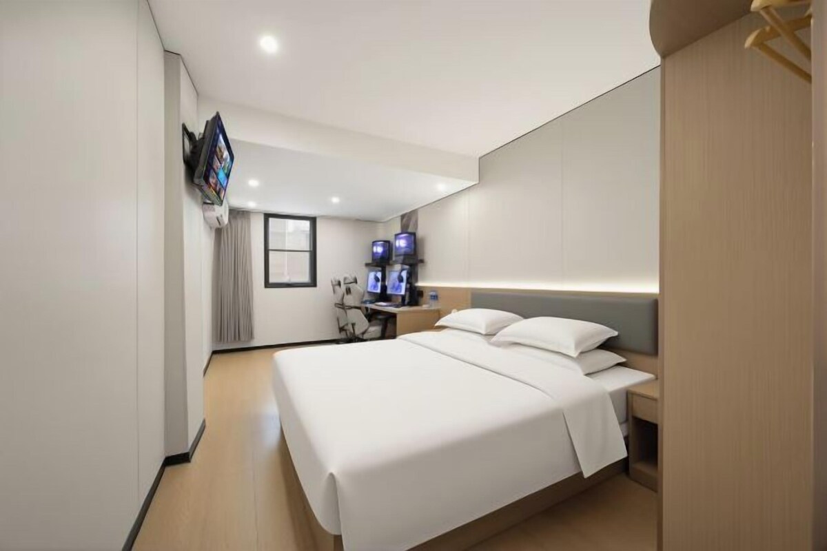 A modern hotel room with a large bed, a flat-screen TV, and a desk with a computer.