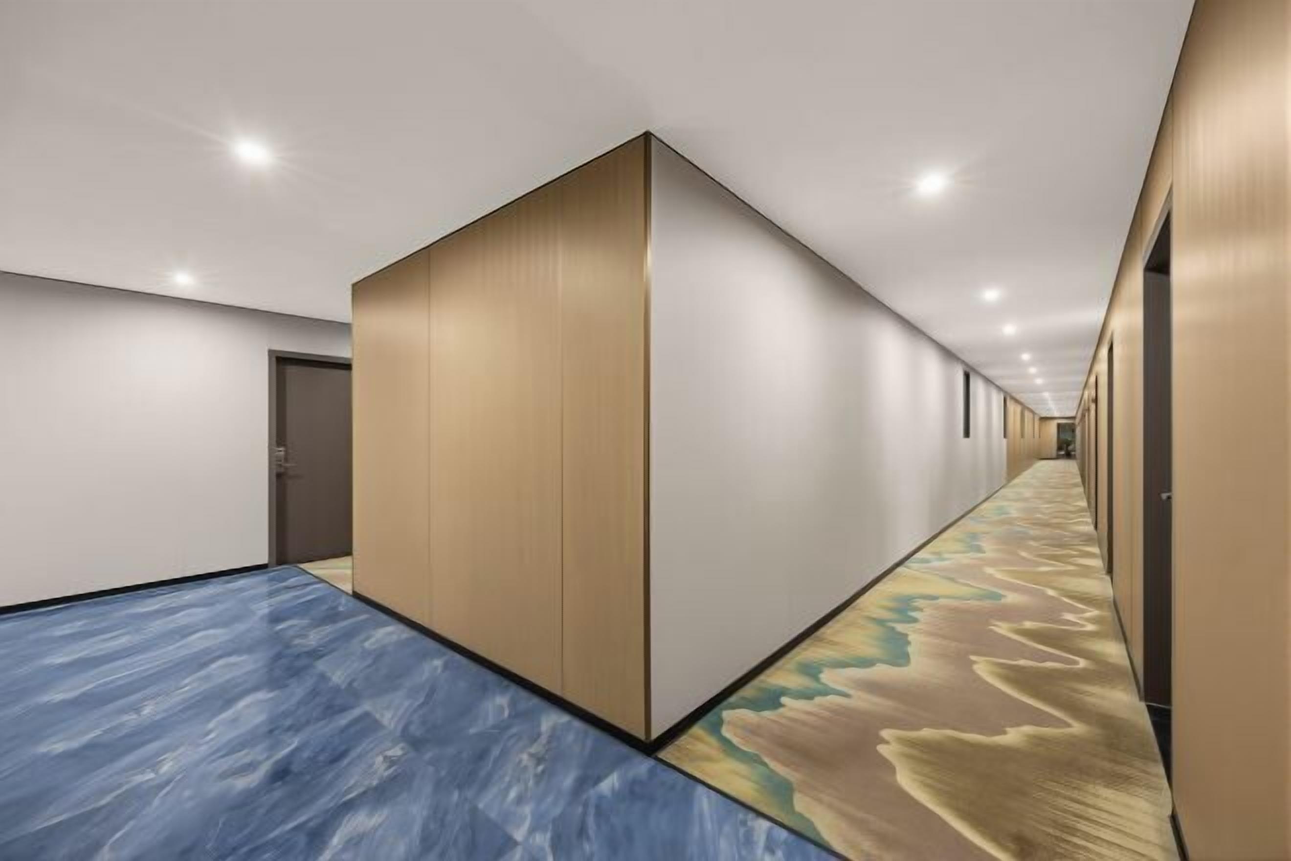 A hotel corridor with a patterned carpet, a wooden partition wall, and a door at the end.