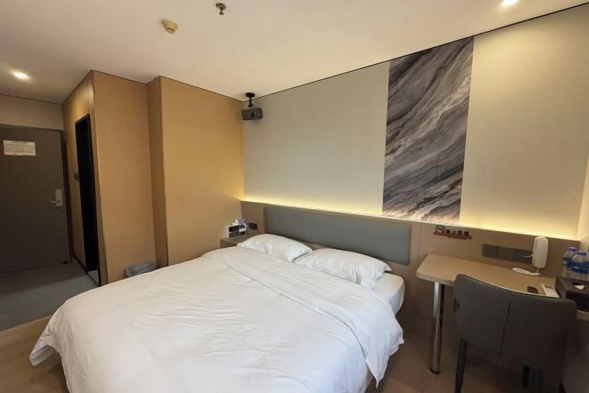 Quarto de hotel com cama, mesa de cabeceira e escrivaninha com cadeira.