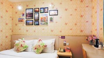 A hotel room with a bed, floral wallpaper, a nightstand with a phone and a vase of flowers, and a wall with framed pictures.