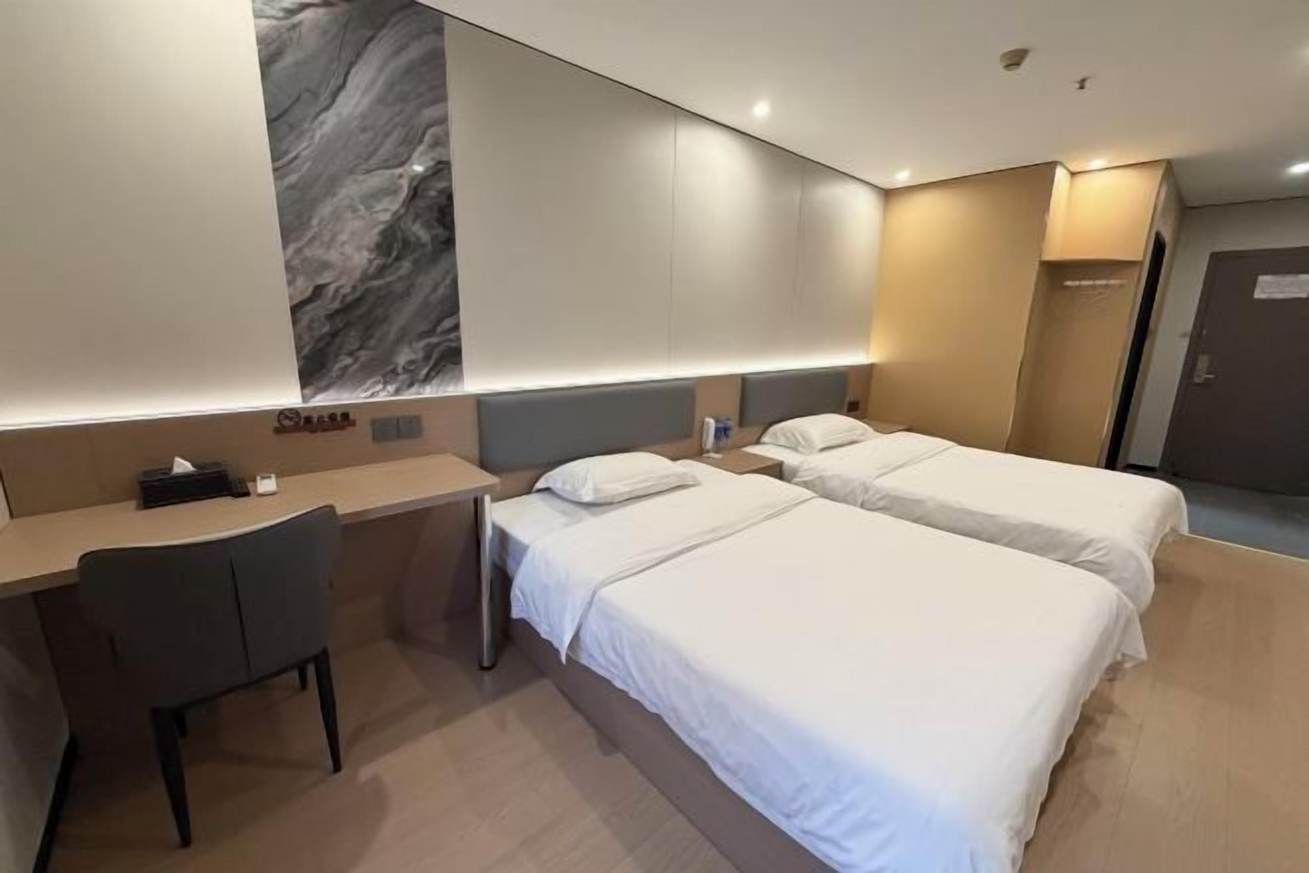 A hotel room with two beds, a desk, and a chair.