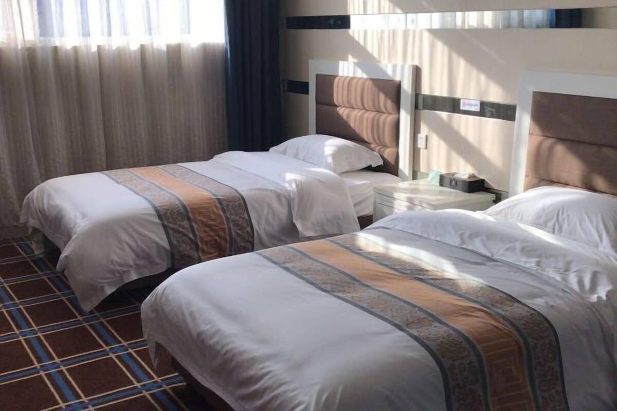 A hotel room with two beds, a nightstand, and a window with curtains.