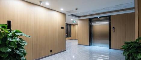 A hallway with wooden panel walls, a marble floor, and two potted plants.