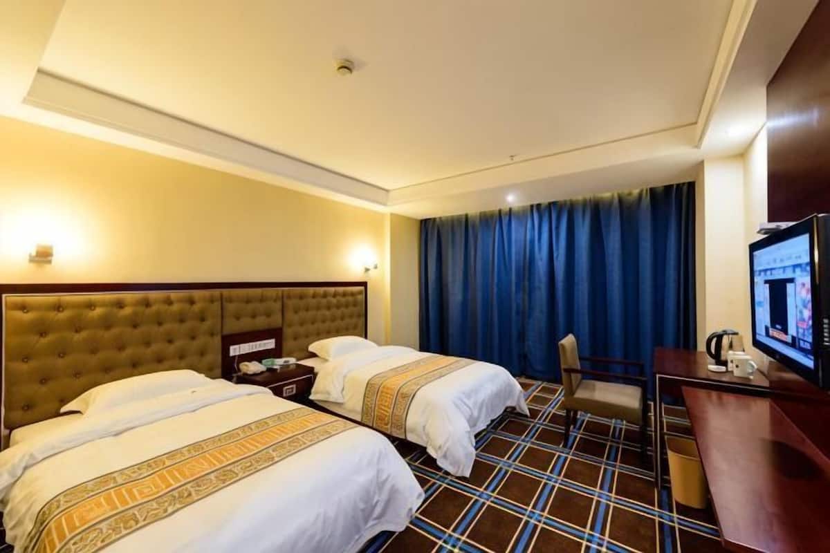 A hotel room with two beds, a TV, a desk, and a chair.