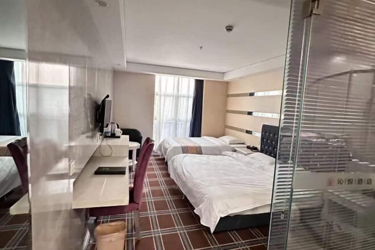 A hotel room with a bed, a desk with a chair, a television, and a window with curtains.