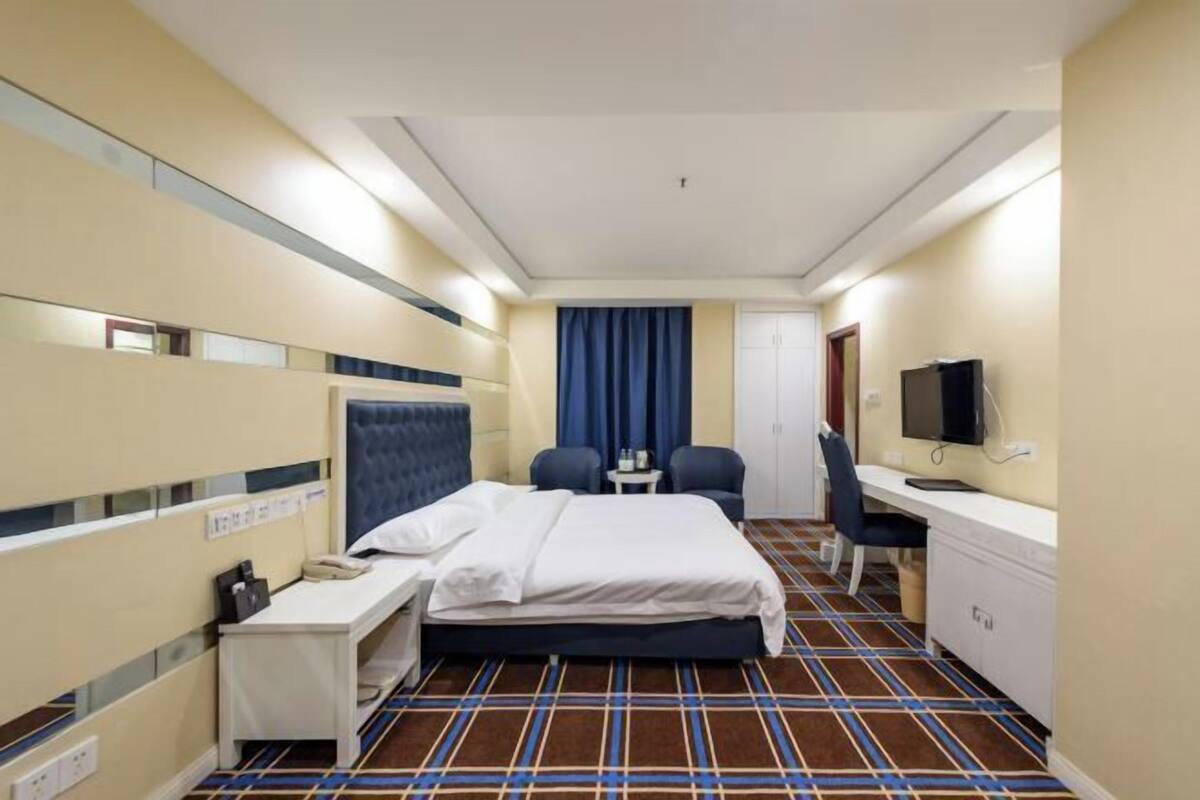A hotel room with a bed, a desk, a chair, a television, and a small table.