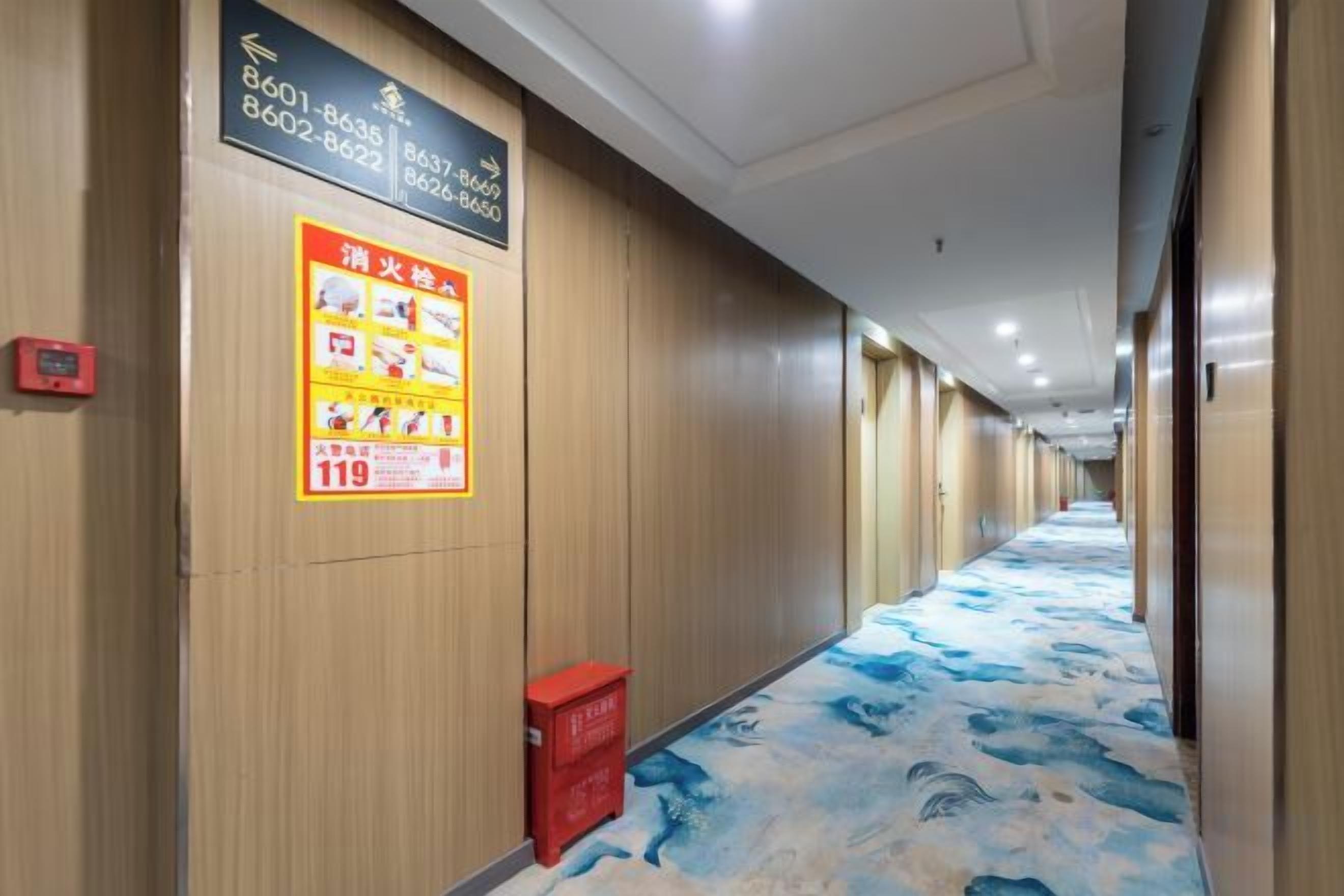 A hotel corridor with wooden walls, a blue and white patterned carpet, and a red trash bin.