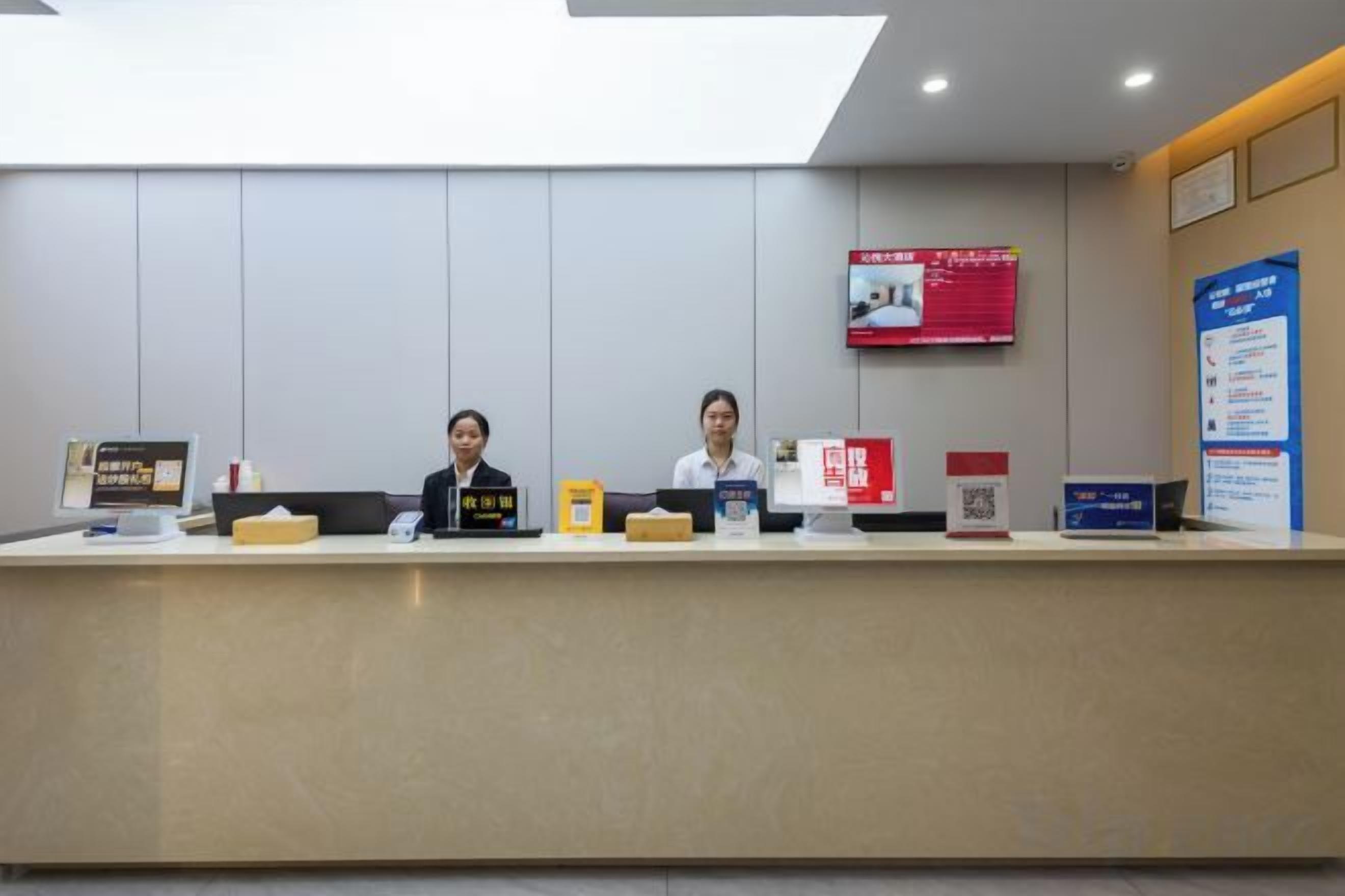 A reception desk with two staff members, a digital information screen, and informational posters.