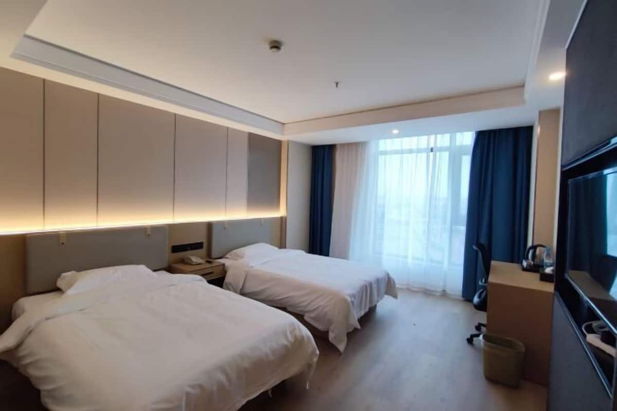 A hotel room with two beds, a large wardrobe, a TV, and a window with curtains.