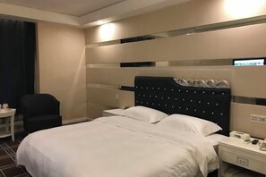 A hotel room with a bed, bedside table, chair, and a wall-mounted control panel.