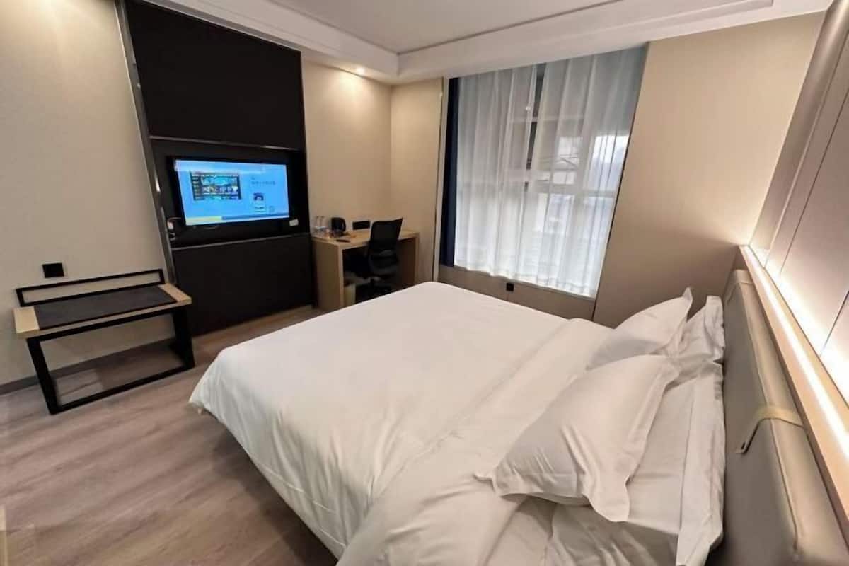 A hotel room with a bed, a desk, a chair, a television, and a window with curtains.