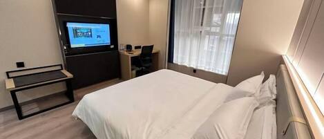 A hotel room with a bed, a desk, a chair, a television, and a window with curtains.