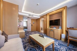 Ein Hotelzimmer mit einem Bett, einem kleinen Tisch, einem Fernseher, einer Küchenzeile und einem gemusterten Teppich.