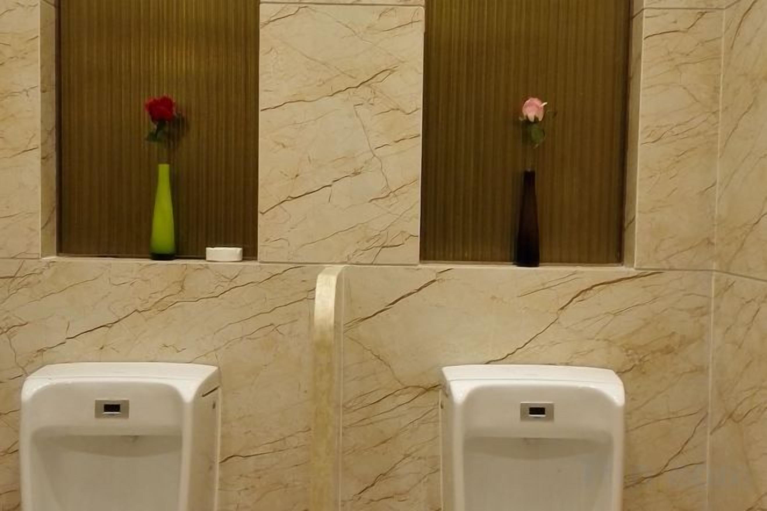 Un baño con paredes de mármol, dos orinales y dos jarrones con flores.