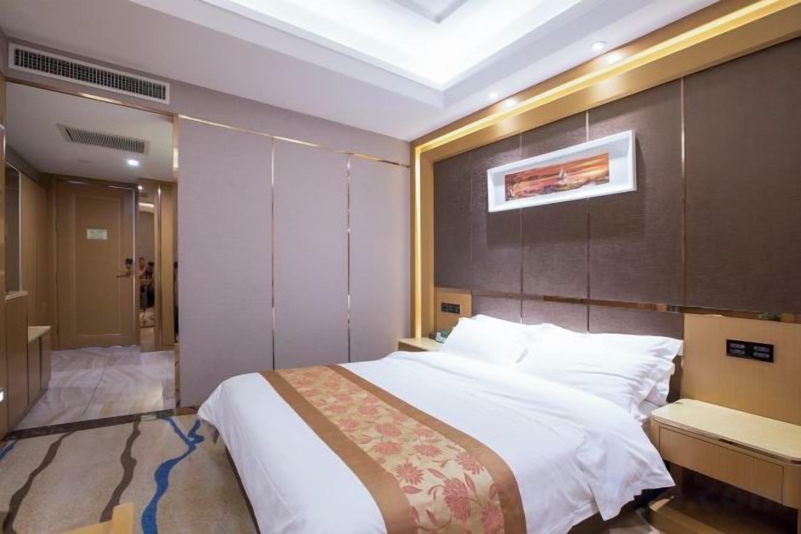 A hotel room with a large bed, bedside tables, a mirror, and a ceiling light.