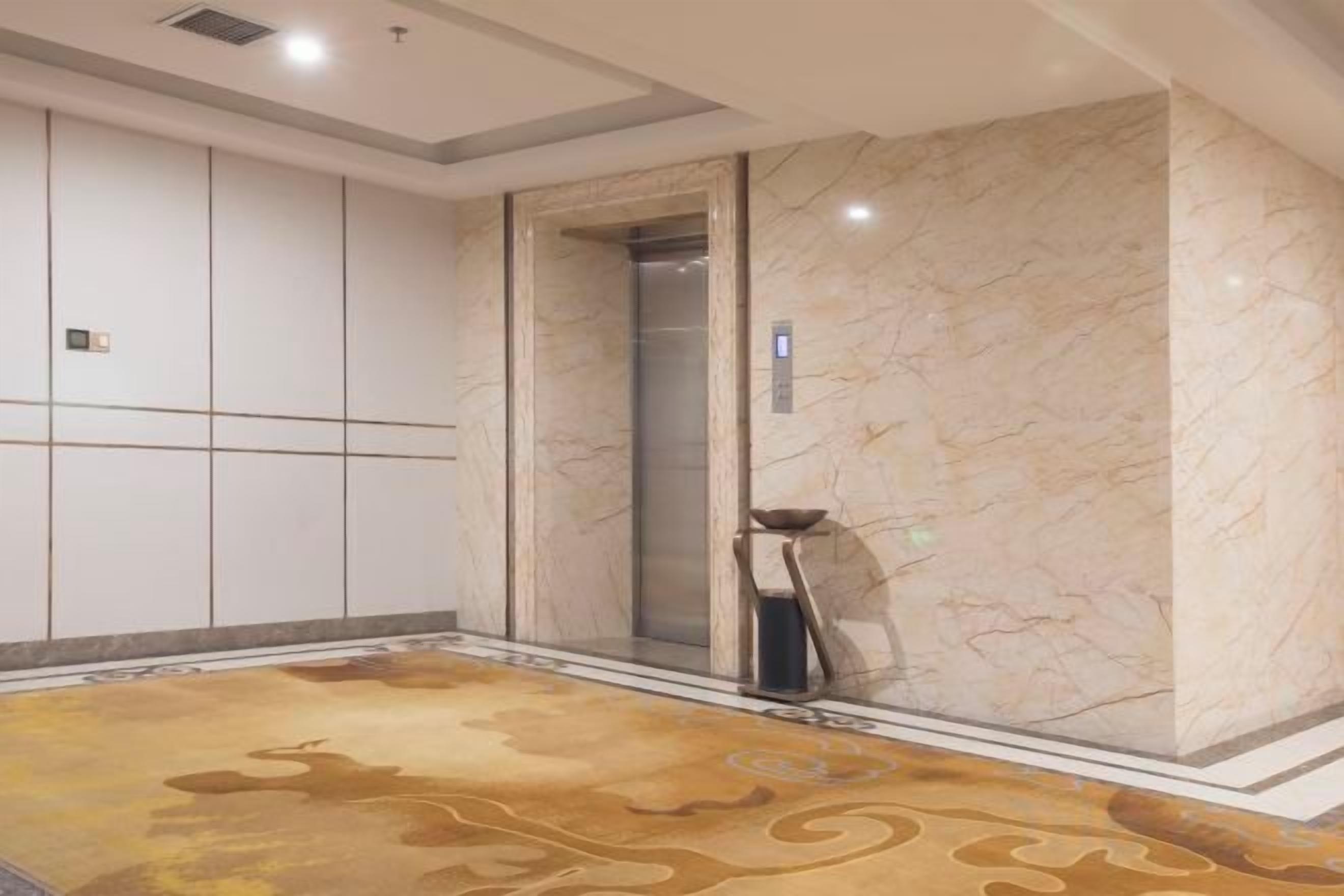 A hotel elevator with marble walls and a patterned carpet.