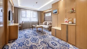 A hotel room with a patterned floor, a sofa, a coffee table, a TV, and a minibar. - Wenzhou Hotel (Hotan City)