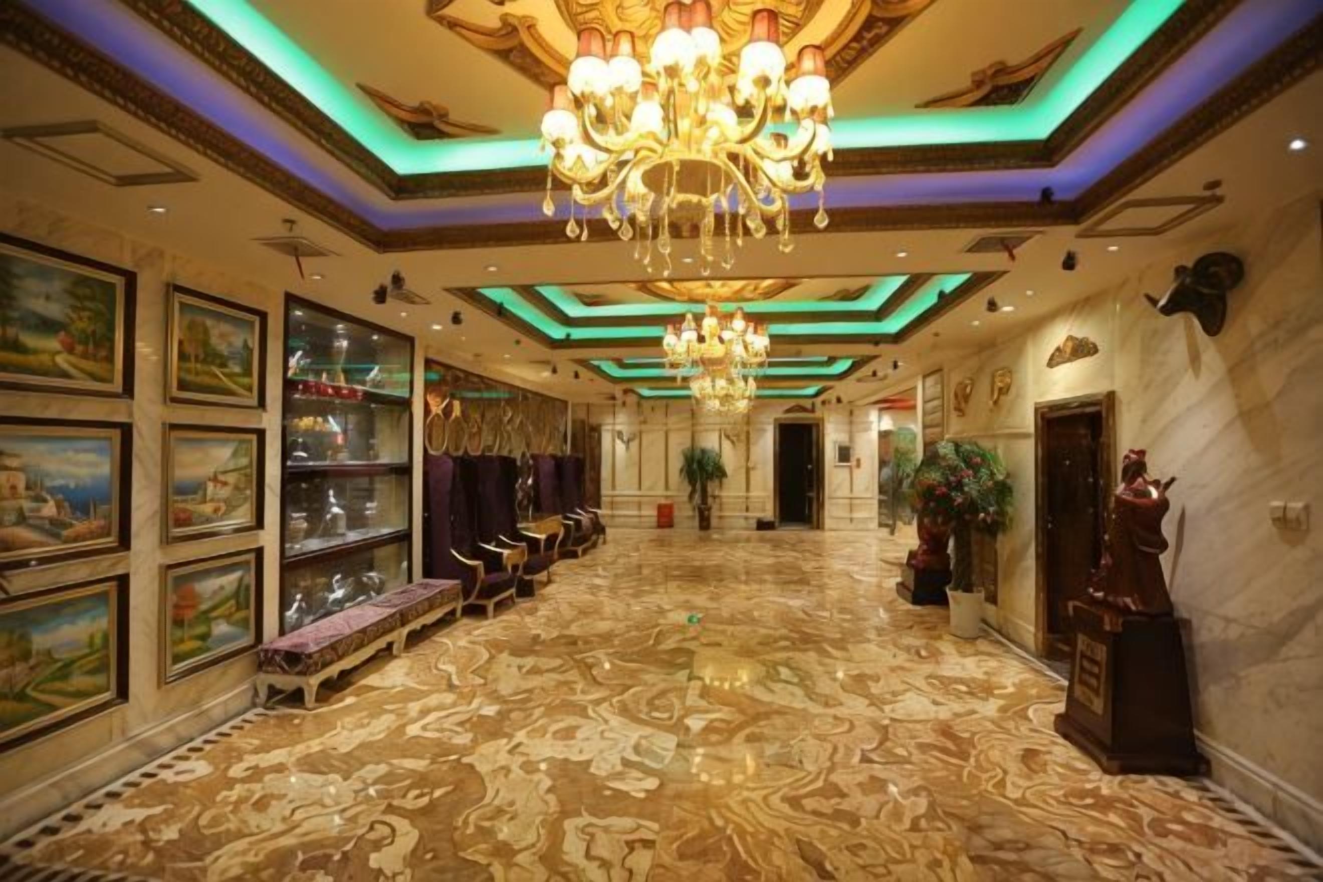 A grand lobby with a chandelier, framed artwork, and a marble floor.