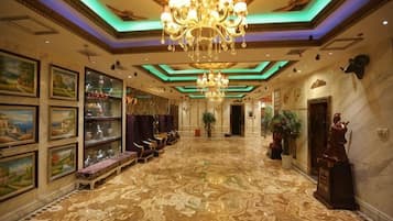 A grand lobby with a chandelier, framed artwork, and a marble floor.