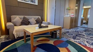 Habitación de hotel con sofá, una mesita, un cesto de basura, alfombra estampada y un armario.