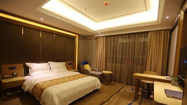 A hotel room with a large bed, a desk, a chair, and a small table. - Wenzhou Hotel (Hotan City)