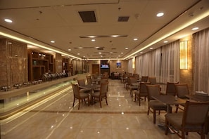 A hotel dining area with a long counter, multiple tables, and chairs.