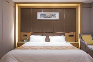 A hotel room with a large bed, a headboard with a framed picture, bedside tables with lamps, and a chair with a cushion. - Wenzhou Hotel (Hotan City)