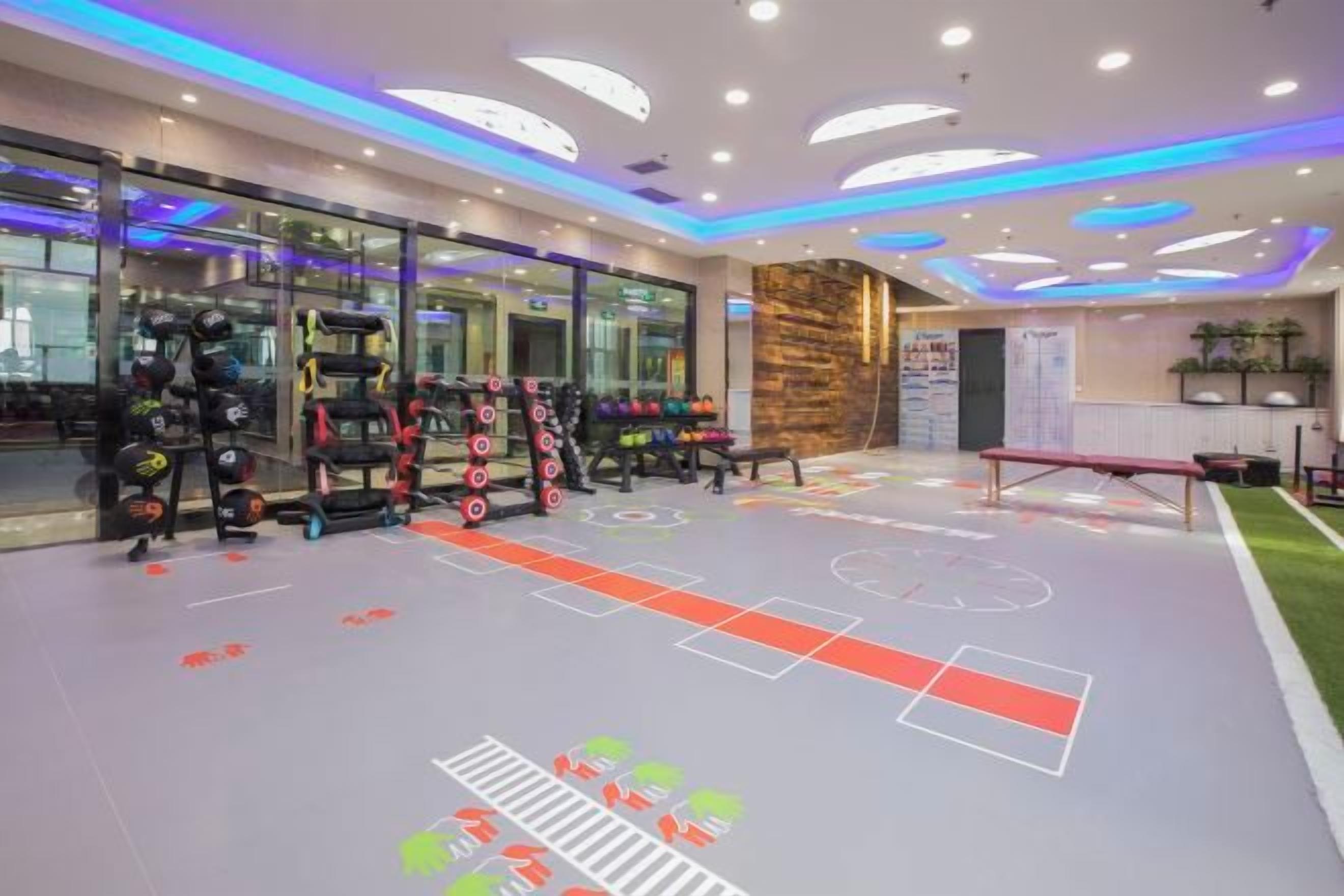 A gym with exercise equipment, a basketball court, and a reception area with a stone wall.