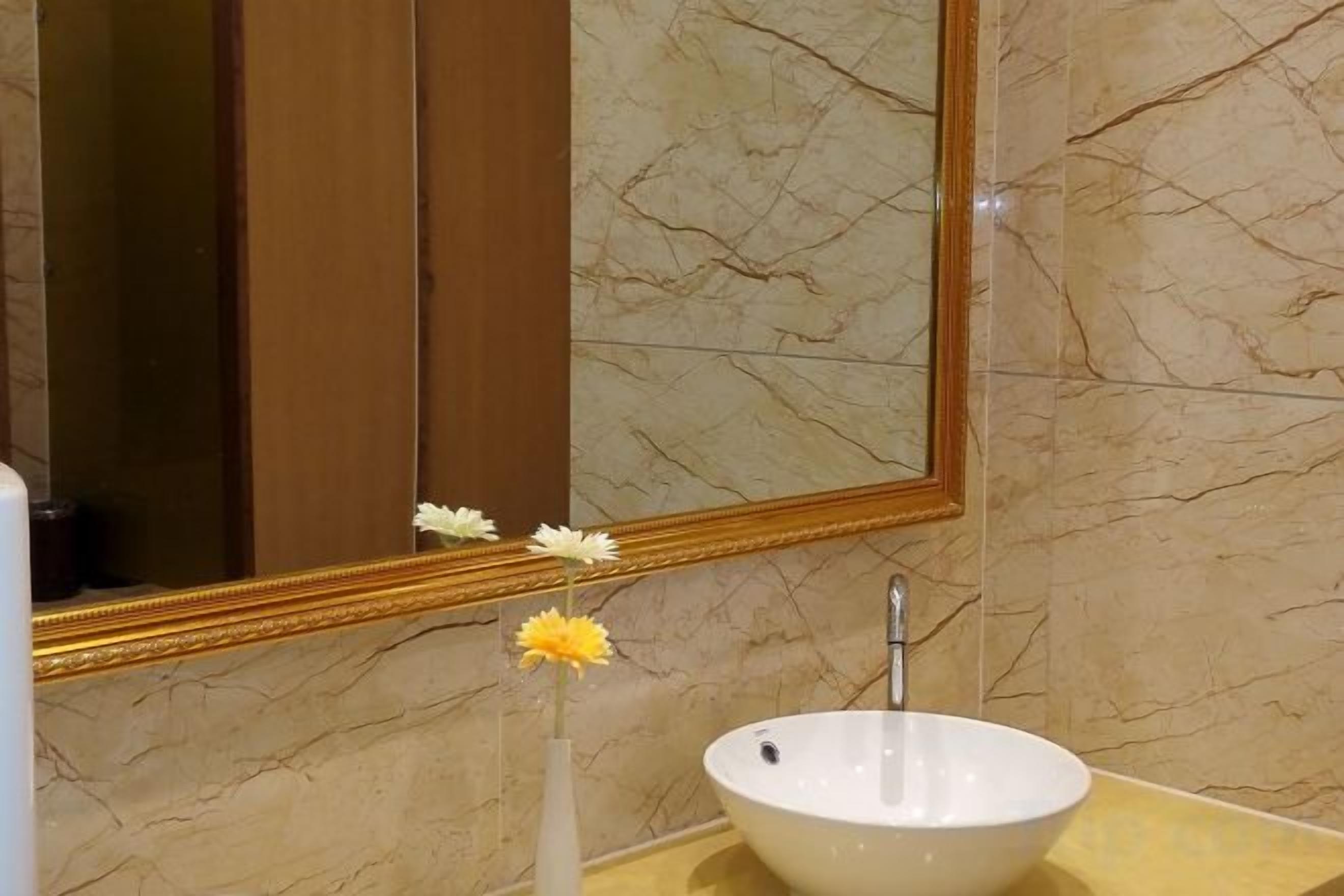 A bathroom with a marble wall, a white sink, and a mirror with a gold frame.