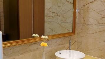 A bathroom with a marble wall, a white sink, and a mirror with a gold frame.
