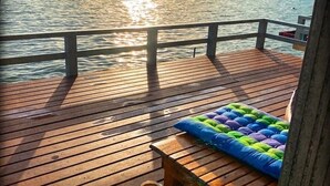 Une terrasse en bois avec une table dressée pour un repas, donnant sur une étendue d’eau au coucher du soleil.