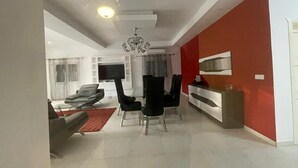 Un salon moderne avec un coin repas, un mur d’accent rouge et un lustre.
