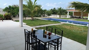 Un patio couvert avec une table et des chaises, une piscine et une végétation luxuriante tout autour.