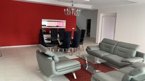 Un salon moderne avec un canapé gris, une table basse en verre et un coin repas agrémenté d’un mur d’accent rouge.