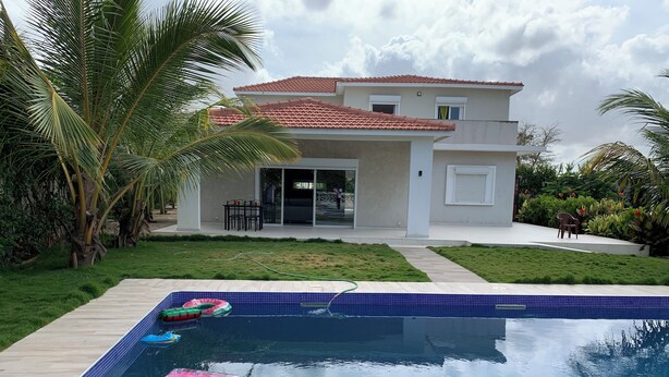 Une maison moderne dotée d’une piscine, entourée d’une pelouse bien entretenue et de palmiers.