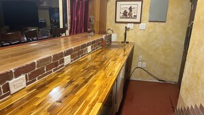 A long wooden bar counter with a brick accent wall, a red curtain, and a framed picture on the wall. - Beautiful 4 bedroom 3.5 bath Home 5 minutes from Down Town Austin. (Austin)