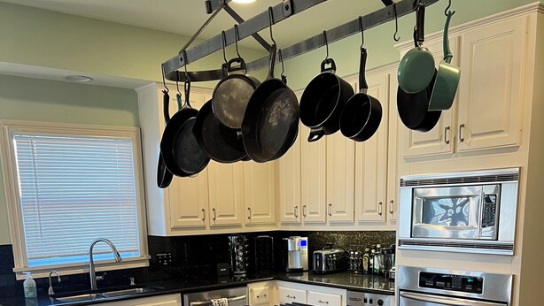 A modern kitchen with white cabinetry, a central island, a hanging pot rack, and built-in appliances including a microwave and oven. - Beautiful 4 bedroom 3.5 bath Home 5 minutes from Down Town Austin. (Austin)