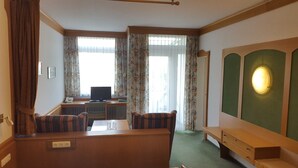 Une chambre d’hôtel avec un lit, un bureau avec un ordinateur, une télévision et une fenêtre avec des rideaux.